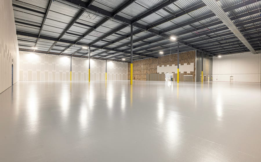 A large coated concrete floor under shop lighting, the finish reflecting the roof structure above it
