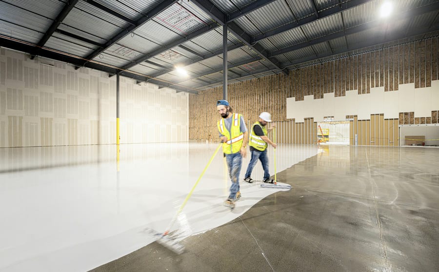 Two installers in high-visibility gear spreading a floor coating across a prepared slab